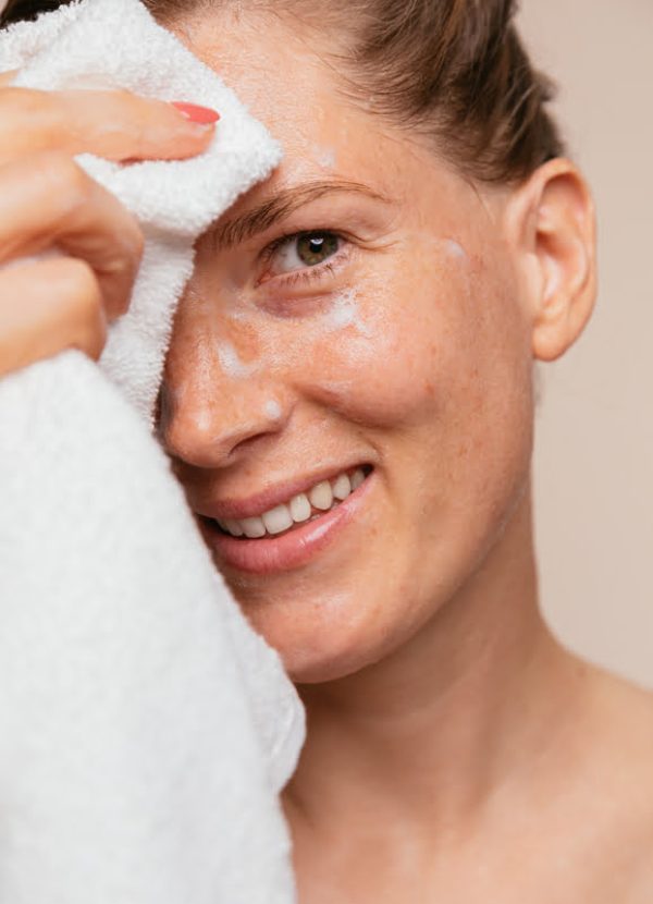 Close Up / Woman cleaning her face and taking of foam from her face with white towel.